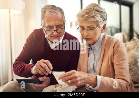 Berechnung unserer täglichen Lebenshaltungskosten. Ein älteres Ehepaar, das ein Budget ausarbeitet, während es auf dem Sofa im Wohnzimmer sitzt. Stockfoto