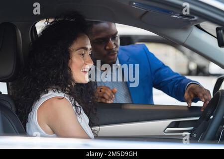 Der schwarze Verkäufer beschreibt die Fahrzeugeigenschaften der Kundin Stockfoto