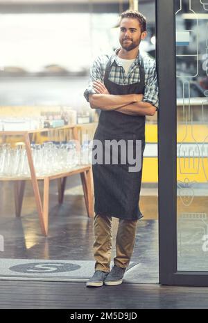 Seine Türen sind offen für Geschäfte. Ein selbstbewusster junger Mann, der in der Tür seines Ladens steht. Stockfoto