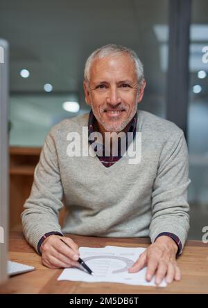 Alles sieht in Ordnung aus. Porträt eines lächelnden, reifen Geschäftsmanns, der Papierkram liest, während er an seinem Schreibtisch in einem Büro sitzt. Stockfoto