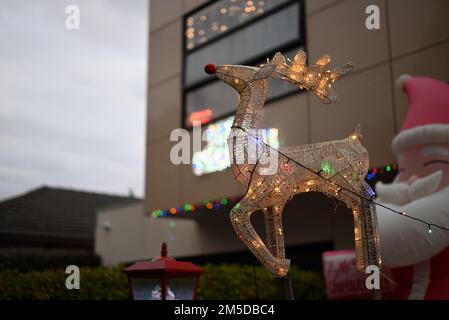 Beleuchtete Vorstadtweihnachtsausstellung mit Rudolph, dem Rentier mit roten Nasen, und anderen festlichen Elementen wie dem Weihnachtsmann im Hintergrund Stockfoto