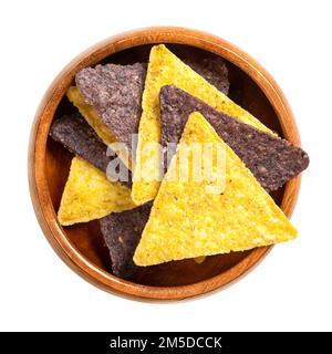 Gelbe und blaue Tortilla-Chips in einer Holzschüssel. Snack aus Maistortillas, die in dreieckige Keile geschnitten, frittiert und leicht gesalzen wurden. Stockfoto