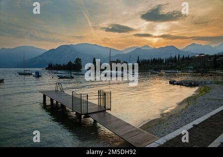 Festgemachte Boote und eine kleine Anlegestelle am Gardasee bei Sonnenuntergang, Malcesine, Italien Stockfoto