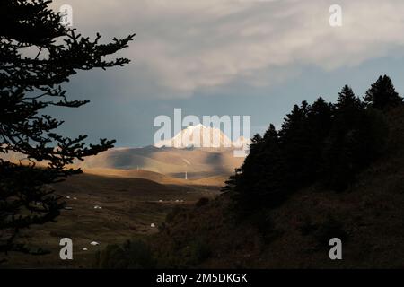 Der Blick auf den schneebedeckten Yala. Hügelige Landschaft mit Bäumen und blauem Himmel. Herbstlandschaft im Grünland. Panoramablick auf die Berge und den Himmel Stockfoto