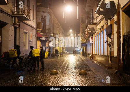 Ternopil, Ukraine - 24. Dezember 2022: Glovo-Kuriere für Lebensmittellieferungen an einem Fahrradstand in der Abendstraße. Stockfoto