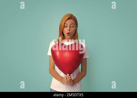 Junges Mädchen mit roten Luftballons. Valentinstag. Isoliert auf blauem Hintergrund. Aufgeregte Frau in der Liebe, fröhliche Emotionen. Stockfoto