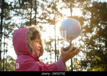Süßes asiatisches Mädchen Lernmodell der Welt mit Naturhintergrund und warmem Sonnenlicht im Park. Kinder lernen durch pädagogische Aktivitäten. Je Stockfoto