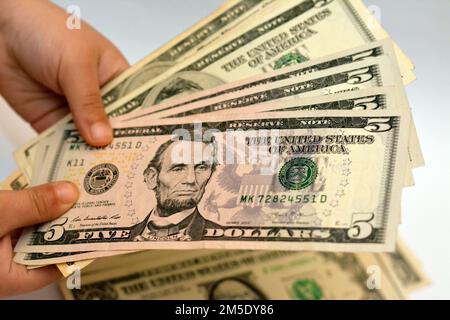 Fünf 5-Dollar-Banknotengeld-Scheine in der Hand eines kleinen Kindes zeigen das Profil eines Porträts von Abraham Lincoln, dem US-Präsidenten von 16., E Stockfoto