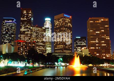 Die Lichter der Skyline von Los Angeles werden bei Nacht beleuchtet, mit einem beleuchteten Springbrunnen davor Stockfoto