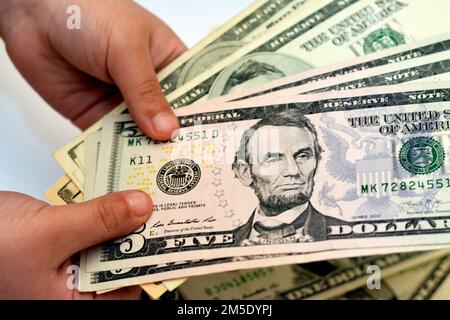 Fünf 5-Dollar-Banknotengeld-Scheine in der Hand eines kleinen Kindes zeigen das Profil eines Porträts von Abraham Lincoln, dem US-Präsidenten von 16., E Stockfoto