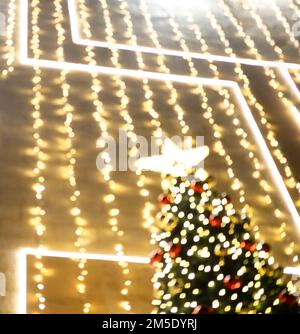 Die Lichter der Girlanden auf dem Weihnachtsbaum mit den roten Kugeln sind unscharf. Stockfoto
