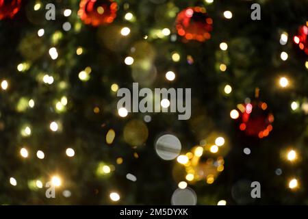 Die Lichter der Girlanden auf dem Weihnachtsbaum mit den roten Kugeln sind unscharf. Stockfoto