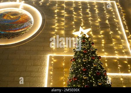 Die Lichter der Girlanden auf dem Weihnachtsbaum mit den roten Kugeln sind unscharf. Stockfoto