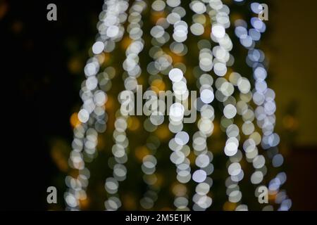 Verschwommene bunte Lichter einer Girlande und Zweige eines Weihnachtsbaums im Vordergrund.Weihnachten und Neujahr Hintergrund.Selektive Fokus, kopieren Spa Stockfoto