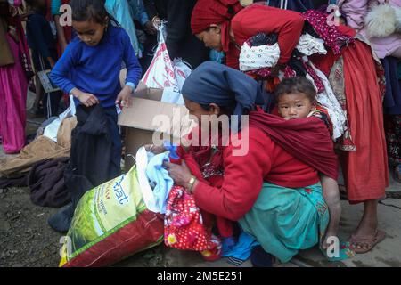 Dhading, Bagmati, Nepal. 27. Dezember 2022. Eine Frau aus der Gemeinde Chepang, die ihr Kind auf dem Rücken trägt, versucht, die gewünschte warme Kleidung für ihre Familie im Dorf Benighat Rorang in Dhading auszuwählen, das am 27. Dezember 2022 etwa 55 km von der Hauptstadt Kathmandu, Nepal, entfernt ist. Heartbeat, eine soziale Organisation zusammen mit einzelnen Spendern, verteilte warme Kleidung und Schreibwaren, Kunstmaterialien an Kinder der Chepang Gemeinde, warme Kleidung an Familienmitglieder. (Kreditbild: © Sunil Sharma/ZUMA Press Wire) Stockfoto