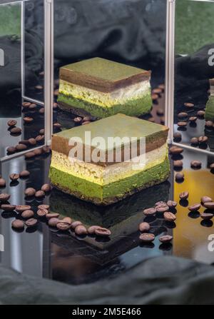 Hausgemachter Käsekuchen mit dunkler Schokolade Matcha und geröstete Kaffeebohnen mit Reflexion im Spiegel werden auf der schwarzen Acrylfolie präsentiert. Stockfoto