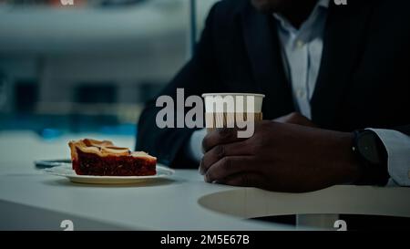 Aus nächster Nähe sehen Sie ein unbekanntes afrikanisches Café, Besucher eines unbekannten Geschäftsmanns im formellen Anzug am Tisch in der Cafeteria, mit einem Kuchenrührer, der Zucker mischt Stockfoto
