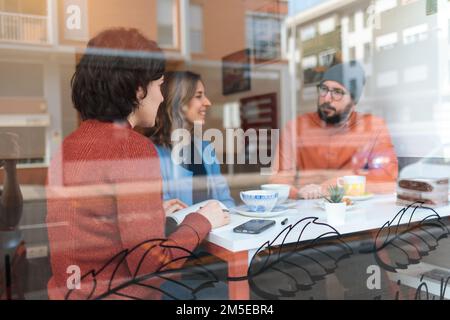 Drei junge Leute sitzen in einem Café, lächeln und reden Stockfoto
