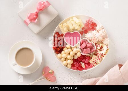 Romantischer Kaffee für zwei, Geschenk, herzförmiger Lollypop und Valentinstagsaufschnitt mit Schokoladenbonbons und Erdbeeren auf weißem Hintergrund. Stockfoto