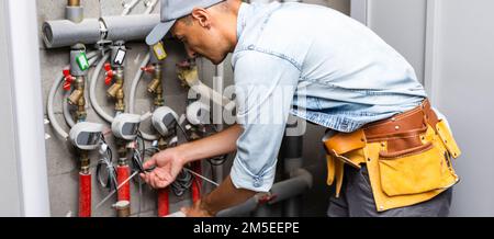 Männlicher Klempner prüft Rohre für zentrale heiß- und Kaltwasserversorgung der Wohnung Stockfoto