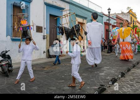Jungs mit kleinen Feuerwerkstieren und riesigen Puppen bei einer Parade während des Guelaguetza-Tanzfestivals in Oaxaca, Mexiko. Die Puppen werden Monos genannt Stockfoto