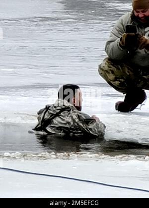 Ein Student in der Cold-Weather Operations Kursklasse 22-05 nimmt am 7. März 2022 an der Schulung zum Eintauchen in kaltes Wasser in Fort McCoy, Wisconsin, Teil. Die Schulung ist Teil des Lehrplans für CWOC. Ein großes Loch im Eis am See wird von CWOC-Mitarbeitern geschnitten, dann folgt ein sicheres und geplantes Regime, damit jeder Teilnehmer in das eisige Wasser springen kann. Notfallpersonal ist auch in der Nähe, falls es benötigt wird. Als jeder Schüler in das eiskalte Wasser stürzte und sicherstellte, dass er auch unter Wasser war, reagierte er sofort. Die CWOC-Studenten werden in einer Vielzahl von Themen für kaltes Wetter ausgebildet Stockfoto