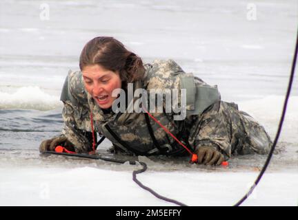 Ein Student in der Cold-Weather Operations Kursklasse 22-05 nimmt am 7. März 2022 an der Schulung zum Eintauchen in kaltes Wasser in Fort McCoy, Wisconsin, Teil. Die Schulung ist Teil des Lehrplans für CWOC. Ein großes Loch im Eis am See wird von CWOC-Mitarbeitern geschnitten, dann folgt ein sicheres und geplantes Regime, damit jeder Teilnehmer in das eisige Wasser springen kann. Notfallpersonal ist auch in der Nähe, falls es benötigt wird. Als jeder Schüler in das eiskalte Wasser stürzte und sicherstellte, dass er auch unter Wasser war, reagierte er sofort. Die CWOC-Studenten werden in einer Vielzahl von Themen für kaltes Wetter ausgebildet Stockfoto