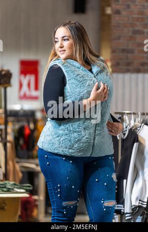 Übergewichtige Frau probiert Kleidung in einem Kleiderladen in der Übergröße-Abteilung an Stockfoto