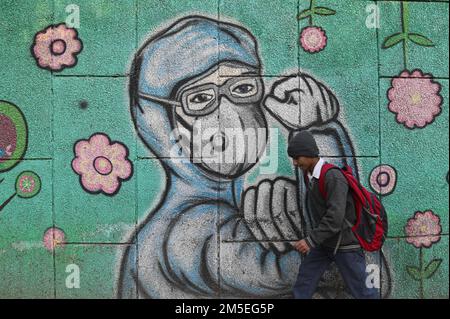 New Delhi, Delhi, Indien. 28. Dezember 2022. Ein Schuljunge geht an einem Graffiti vorbei, das Covid-19-Coronavirus-Krieger mit Gesichtsmasken an einer Straße in Neu Delhi zeigt. (Bild: © Kabir Jhangiani/ZUMA Press Wire) Stockfoto