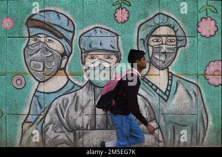 New Delhi, Delhi, Indien. 28. Dezember 2022. Ein Schuljunge geht an einem Graffiti vorbei, das Covid-19-Coronavirus-Krieger mit Gesichtsmasken an einer Straße in Neu Delhi zeigt. (Bild: © Kabir Jhangiani/ZUMA Press Wire) Stockfoto