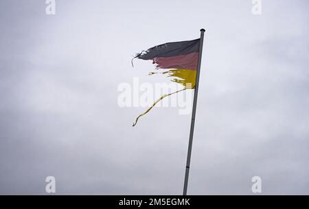 Bad Vilbel, Deutschland. 28. Dezember 2022. Eine deutsche Flagge, zerrissen vom Wind und verblasst vom Licht, flattert auf dem Dach eines Hauses. Kredit: Frank Rumpenhorst/dpa/Alamy Live News Stockfoto