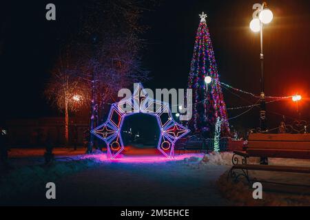 Weihnachtsbaum bei Nacht schneit es, die Lichter sind an Stockfoto
