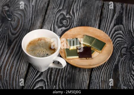 Eine Tasse schwarzen Kaffee in einer weißen Tasse. Schokolade in Folie. Auf Pinienbrettern. Stockfoto