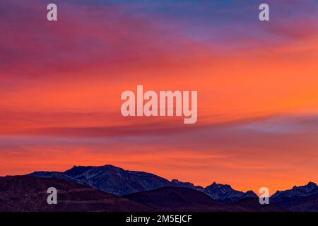 Die untergehende Sonne erhellt die Wolken über den schneebedeckten Bergen in der Nähe von Bishop in Kalifornien, USA Stockfoto