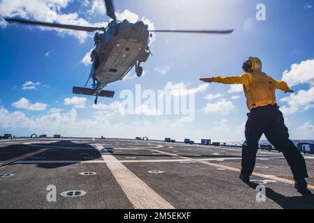 220308-N-GF955-1129 KARIBISCHES MEER - (8. MÄRZ 2022) -- Mineman 1., Klasse Daniel Leno, dem Küstenschiff USS Billings (LCS 15) in der Freiheitsvariante zugeteilt, signalisiert die Landung eines MH-60s Sea Hawk Hubschraubers, der dem ‚Shadow det‘ des Helicopter Sea Combat Squadron (HSC) 28, Einheit 7, auf dem Cockpit, 8. März 2022, zugewiesen wurde. Billings wird in das US-Flottengebiet 4. entsandt, um die Mission der Joint Interagency Task Force South zu unterstützen, zu der auch Missionen zur Bekämpfung des illegalen Drogenhandels in der Karibik und im östlichen Pazifik gehören. Stockfoto