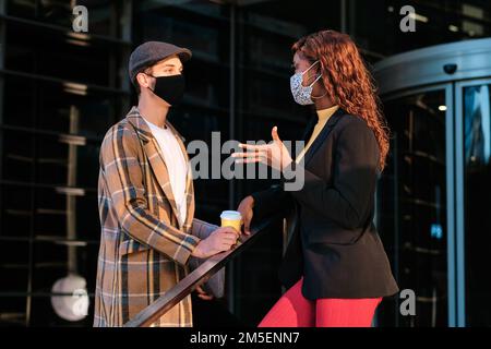 Zwei Geschäftsleute mit Gesichtsmaske, die sich vor dem Bürogebäude unterhalten. Stockfoto