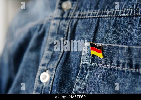 Ein Metallabzeichen mit der deutschen Flagge ist auf einer blauen Jeans-Jacke befestigt. Stockfoto