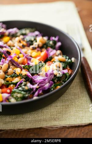 Farbenfroher schwarzäugiger Erbsen- und Grünkohlsalat mit Quinoa, Mais, Paprika, Karotten und Purpurkohl. Stockfoto