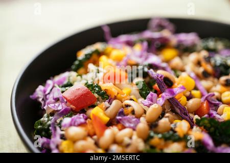 Farbenfroher schwarzäugiger Erbsen- und Grünkohlsalat mit Quinoa, Mais, Paprika, Karotten und Purpurkohl. Stockfoto