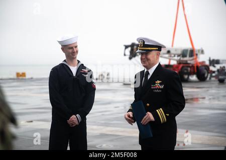 Leutnant Cmdr. Eric Melvin, richtig, der Kaplan von 30 des Fleet Logistics Multi-Mission Squadron (VRM) aus Pensacola, Florida, hält eine Rede vor Seeleuten, die der Medienabteilung von USS Gerald R. Ford (CVN 78) zugewiesen wurden, nachdem sein Sohn, Mass Communication Specialist 2. Class Zachary Melvin, wieder in die USA zurückversetzt wurde Navy auf Fords Flugdeck, 15. März 2022. Ford liegt im Hafen der Marinestützstelle Norfolk und führt vor dem ersten Einsatz des Schiffes eine maßgeschneiderte Grundphase durch. Stockfoto