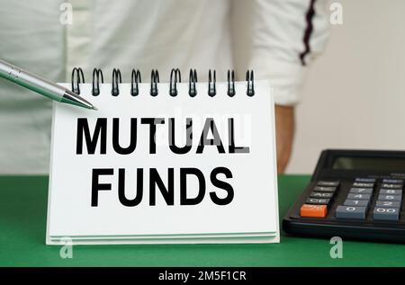 Geschäftskonzept. Auf einer grünen Oberfläche ist ein Taschenrechner, ein Mann zeigt mit einem Stift auf ein Notizbuch mit der Aufschrift "Mutual Funds" Stockfoto