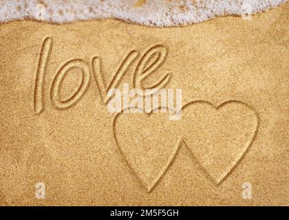 Worte in Strandsand geschrieben. Das Wort LIEBE im Sand am Strand mit dem Ozean als Hintergrund geschrieben. Liebe ist alles, was du brauchst. Jeder liebt das Stockfoto