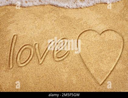 Worte in Strandsand geschrieben. Das Wort LIEBE im Sand am Strand mit dem Ozean als Hintergrund geschrieben. Liebe ist alles, was du brauchst. Jeder liebt das Stockfoto