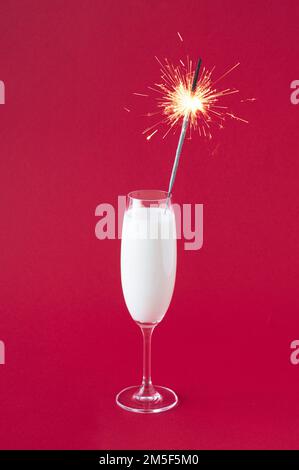 Milch in einem Champagnerglas auf rot-violettem Hintergrund. Silvester-Glitzer im Glas. Weihnachtskonzept für Partyfeiern. Stockfoto