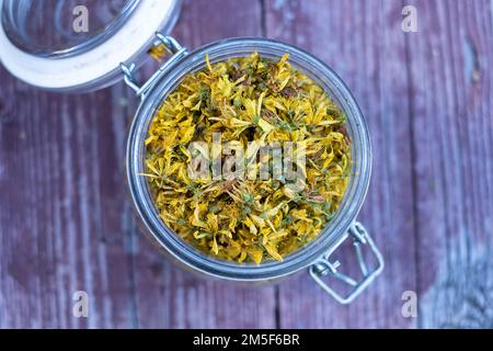 Glasgefäß mit trockenen Johanniskraut- oder Hypericum perforatum-Blütenblättern auf altem Holzhintergrund. Stockfoto