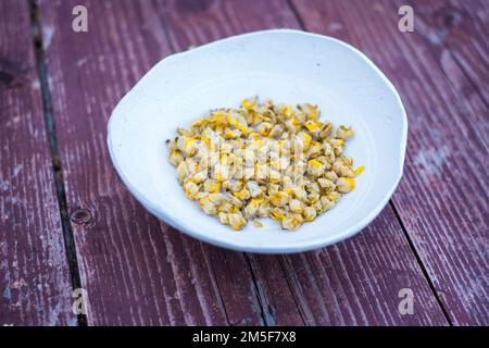 Trockener Kräutertee aus großen Mulleinblüten oder Verbascum thapsus in einer kleinen Tonschüssel mit Holzhintergrund. Stockfoto