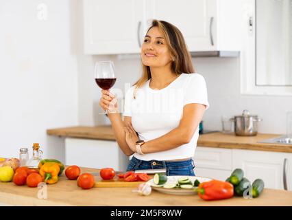 Positive junge Latina Kochen und Wein trinken in gemütlicher Küche Stockfoto