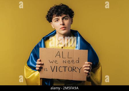 Ein ukrainischer Mann mit Pappe alles was wir brauchen ist ein Sieg auf gelbem Hintergrund. Die Ukraine wird den Krieg gewinnen. Demokratie, Freiheit, Demonstration, russische Aggresion Stockfoto