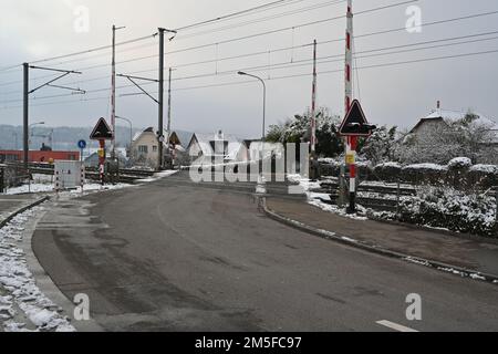 Bahnübergang im Dorf Urdorf im Winter, mit offenen Barrieren gefangen. Stockfoto