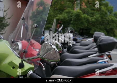 Detaildarstellung von Mopeds verschiedener Farben, die in Reihe geparkt sind, mit Fokus auf dem ersten Motorrad. Stockfoto